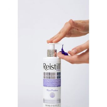 Close-up of hand dispensing Reistill Blonde Creator purple conditioner, anti-yellow brightening formula with rice protein, 250 ml bottle for blonde and grey hair